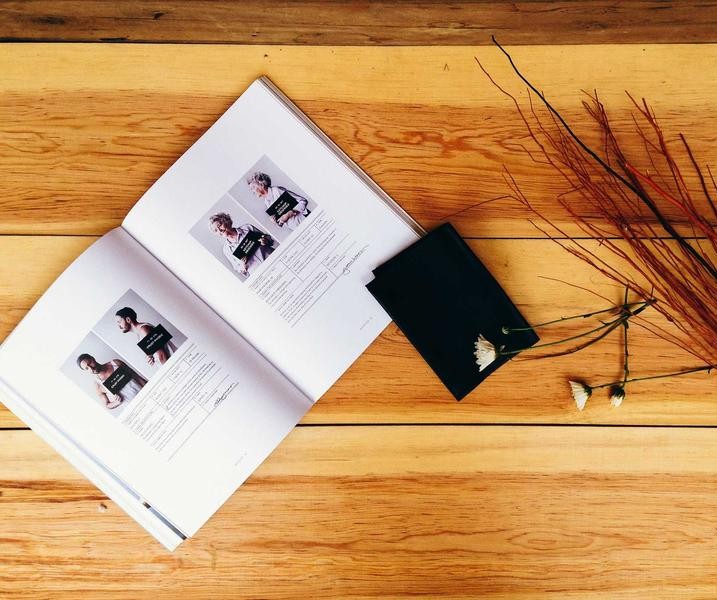 Open book and black journal on a wooden table with dried branches and small white flowers